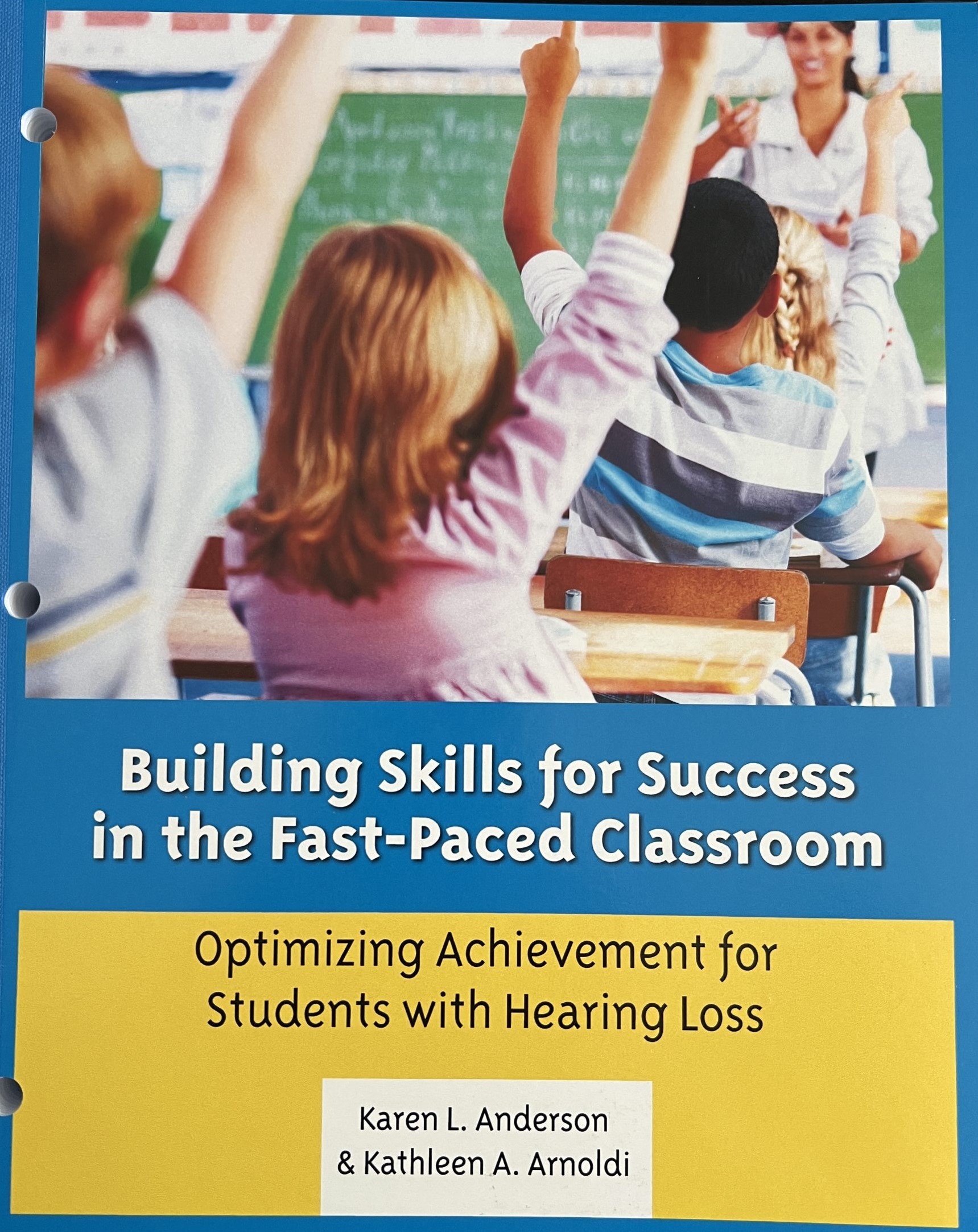 The cover of the book "Building Skills for Success in the Fas-Paced Classroom" features the title in the center on a blue background. Above, a group of students are sitting in a classroom raising their hands with a smiling teacher standing at the front of the room.