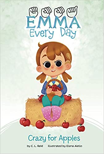 The cover of the book "Emma Everyday: Crazy for Apples" features a green background and the title at the top. An illustrated smiling little girl wearing a cochlear implant processor sits on a hay bale surrounded by apples on the ground.