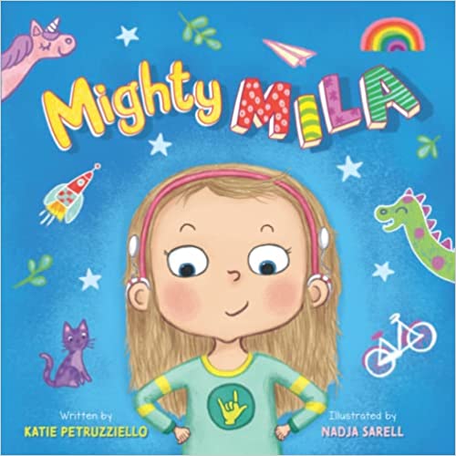 The cover of the book "Mighty Mila" has an illustrated bright blue background with white stars and green leaves and the title across the top. A smiling young girl stands in the middle with her hands on her hips wearing a pink headband, two white cochlear implant processors, and a green shirt with the sign for "I Love You" in the center.
