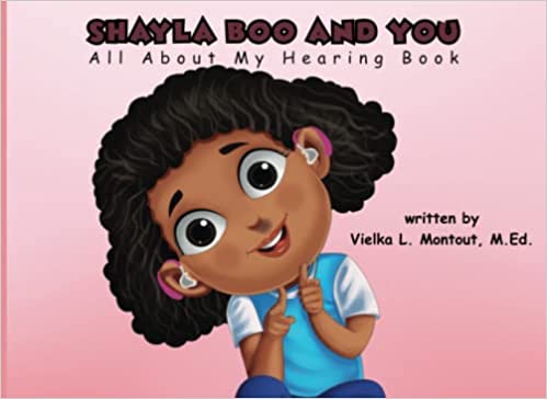 The cover of the book "Shayla Boo and You: All About My Hearing Book" features a pale pink background with the title across the top. An illustrated smiling young girl with dark brown wavy hair is in the center wearing two pink hearing aids and pointing with both hands towards the reader.
