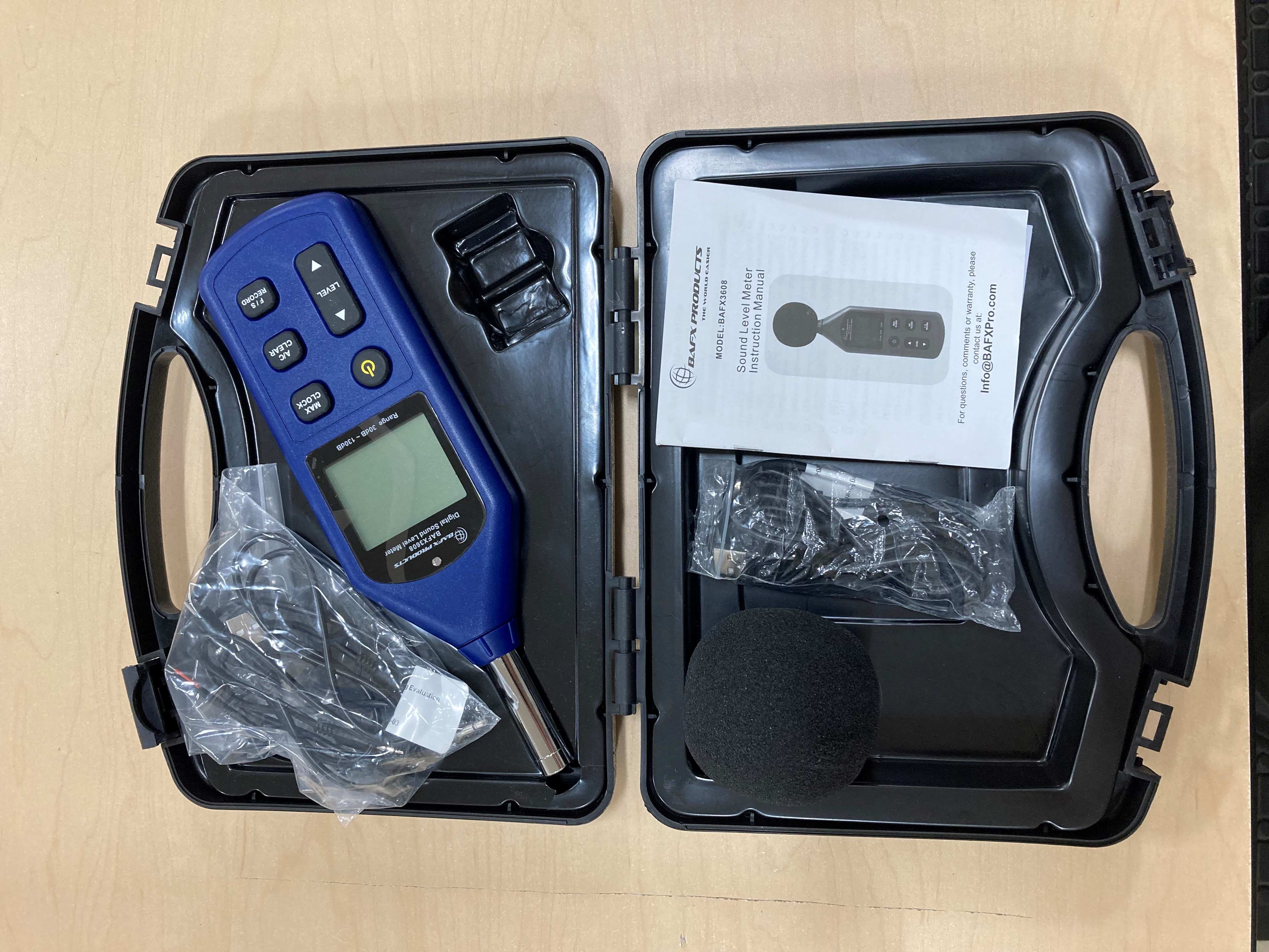 A black, hard-sided case containing a sound level meter and charging cords.