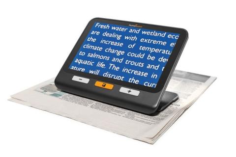 A small device with a screen. The device is resting on a newspaper and the screen is magnifying the text.